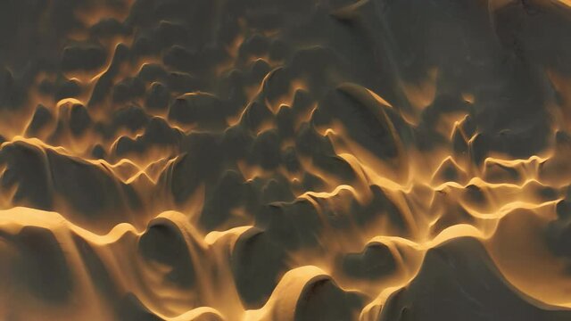 4K abstract background of wavy shapes and patterns on sand hills. Beautiful top down drone view flying above the scenery landscape of massive golden dunes at sunset. Wild desert nature, California USA