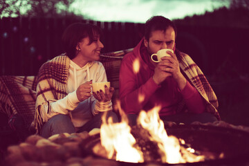 Romantic weekend. Couple In Love Near Camping In Nature. Portrait Of Lovely Happy Man And Beautiful Woman Hugging And Resting Near Bonfire On Vacation Outdoors at night. togetherness concept