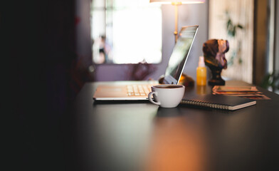 Workplace on desk. close-up white coffee cup,  notepad  and laptop.  Dark tone and color lighting...