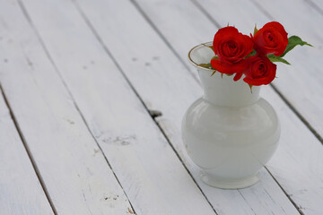 Red roses in a white vase on vintage white old table