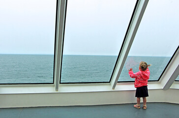 Little Caucasian curious girl is standing by the big glass window while being on ferry to Vancouver Island.