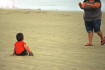 Mom is spooking her indigenous cute little son sitting on a sandy beach in Tofino, Vancouver Island.