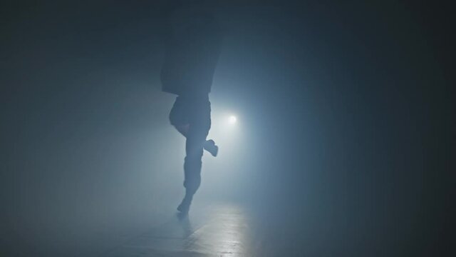 Silhouette of talented woman dancer dancing hip hop in smoky studio. Young female dancing on stage with smoke and spotlight in 4K, UHD