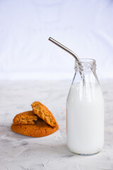 Glass bottle with milk and cocktail straws, oatmeal cookies on a white concrete background. The concept of home breakfast and healthy eating.