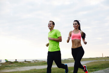 Portrait of cheerful Caucasian couple running outdoors, beautiful young couple working out near the beach jogging in nature