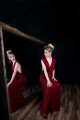 beautiful girl in evening burgundy dress by the mirror with her reflection on a black background