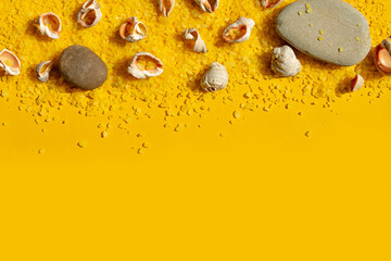 Seashells and stones on a bright yellow sandy background. Summer background with bright sunlight. Travel and vacation concept