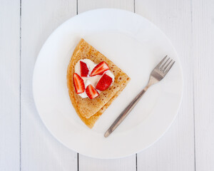 Crepes with strawberries on a white plate on a wooden table. Top view