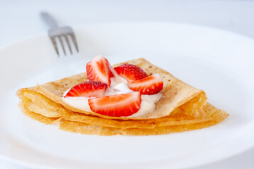 Crepes with strawberries on a white plate on a wooden table