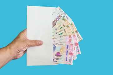 female hand holds a white envelope with hryvnia / isolated on a blue background. 200, 500, 1000 hryvnias. Financial concept.