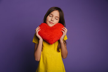 Photo of pleased girl holding soft toy heart with eyes closed
