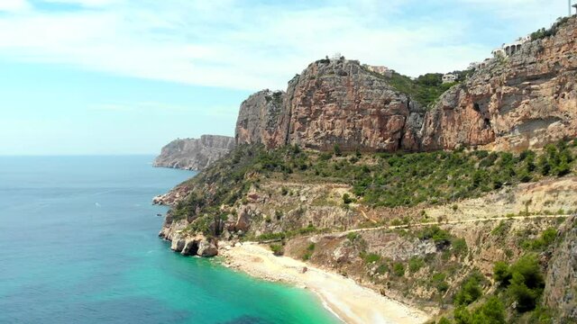 Aerial drone point of view picturesque Cala de Moraig in Benitachell coastal town. Bright turquoise waters bay of Mediterranean Sea empty white sandy beach, huge cliffs coastline. Costa Blanca. Spain