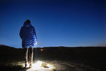 Mujer joven sentada observando el cielo estrellado en la montaña de Sierra Nevada