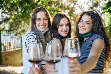 Young millennial women toasting in a park with red wine glasses in a tasting of a restaurant - Group of people having fun together - Friends taking a memories photo in a relax moment