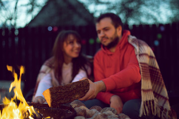 Loving man and woman on romantic party by bonfire, young man adds wood to fire selective focus. Romantic Weekend. Couple In Love Near Camping In Nature. concept togetherness