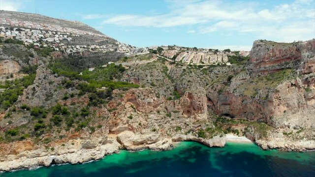 Aerial drone point of view picturesque Cala de Moraig in Benitachell coastal town. Bright turquoise Mediterranean Sea lagoon empty white sandy beach, huge cliffs idyllic coastline. Costa Blanca. Spain
