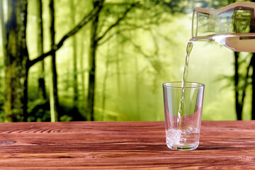 Drink water pouring in to glass over natural green forest background