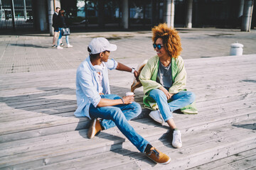 Cheerful young afro american family having fun spending leisure together walking lovely pet on spring sunny day, trendy dressed hipsters friends joking while communicating sitting on urban settings