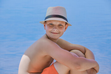 Fototapeta premium Baby summer sits on the beach in a hat on the sea
