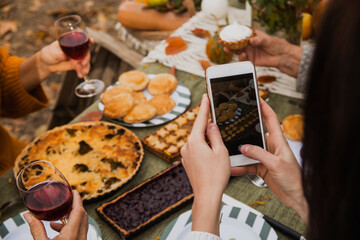 A young girl takes a photo of a festive family table on a smartphone. Autumn brunch in the backyard.