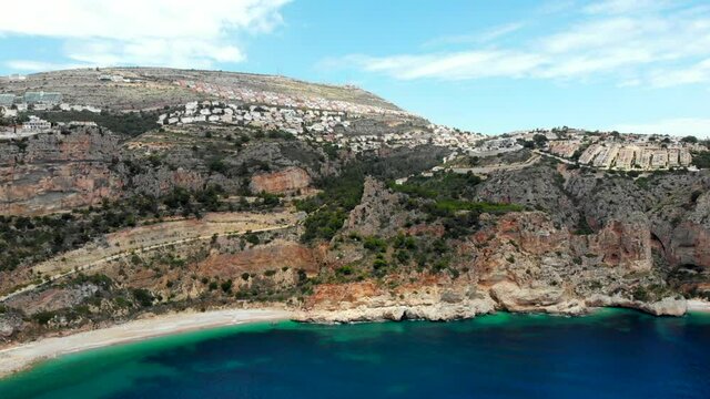 Aerial drone point of view picturesque Cala de Moraig in Benitachell coastal town. Bright turquoise Mediterranean Sea lagoon empty white sandy beach, huge cliffs idyllic coastline. Costa Blanca. Spain