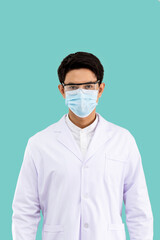 Portrait of confident male Asian researcher scientist medical doctor wearing surgical mask and protection glasses standing isolated on light green background