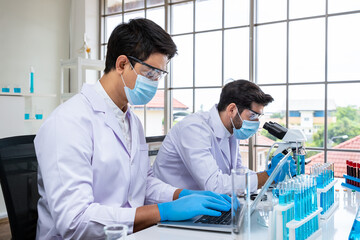 Two male Asian and Arab researcher scientists working in laboratory, conducting study biohazard substance with scientific equipment and microscope