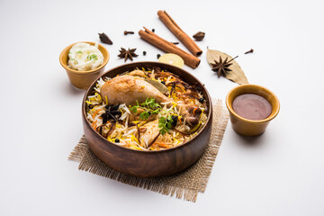 Restaurant style Spicy Chicken Biryani in wooden bowl with Raita and salan, Popular Indian or...