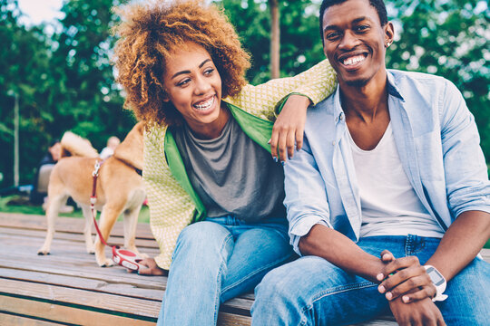 Cropped image of good looking afro american couple dressed in stylish clothes fooling around during summer walk at street.Positive man and woman friends laughing and joking during sitting on bench