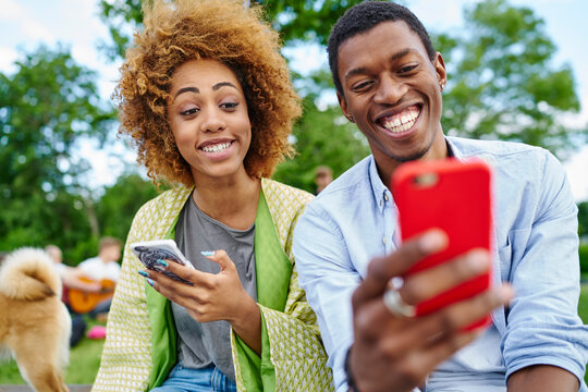 Positive african american friends with funny grimaces on face looking at front camera of modern smartphone and making selfie photos for blog spending together free time in urban setting