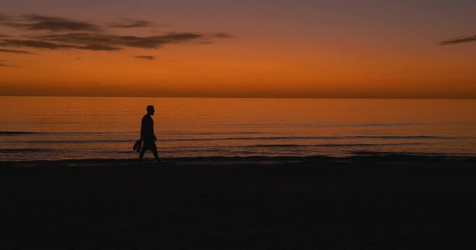 500 Silhouette of a man walking in the water holding his shoes after the sun has set