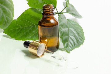 Glass cosmetic bottles with a dropper stand next to green leaves on a white background. Organic cosmetics concept, natural essential oil and cream.