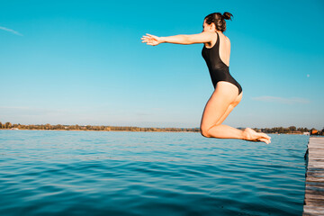 woman jumping from wooden pier in lake water
