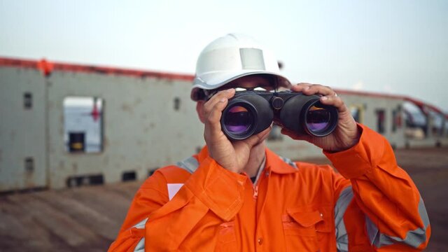 Filipino deck Officer on deck of vessel or ship , wearing PPE personal protective equipment. He is looking through binoculars.