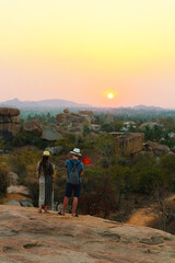 Sunset Point at Hampi. The girl and the guy in hats admire the sunset. Golden evening in India.
