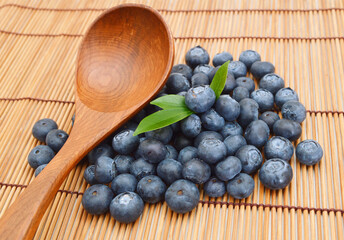 heap of blueberries with mint leaf and wooden spoon isolated on bamboo mat background
