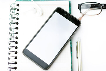 Workspace, on the office desk is a notebook, phone and glasses.