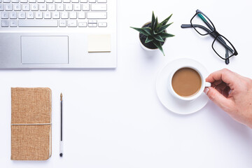 Flat lay, Workplace with laptop, hand taking coffe and notebook and pen on withe desk.