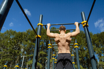 An athletic man does pull-UPS on a horizontal bar on a sport ground in the Park. The view from the...