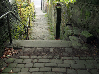 old outdoor stone steps in dark alley with cobblestones and moss growing on the walls