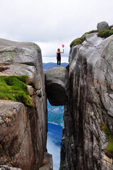 Girl standing on the stone Kjeragbolten between mountains in Norway