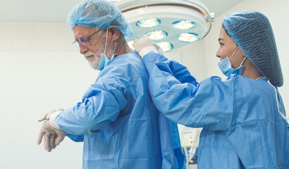 Female assistance helping senior doctor wearing operation uniform