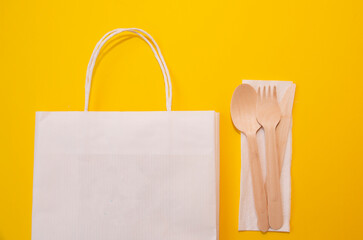 paper bag and cutlery on a yellow background. Shopping, eco packaging or delivery concept.