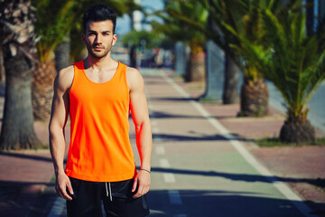 Half length portrait of muscular build handsome male posing for the camera outdoors, handsome runner in bright t-shirt resting after workout, copy space area for your text message or advertise content