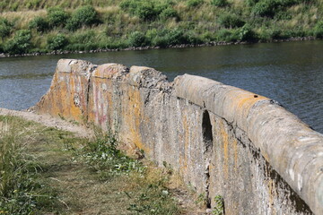 The destroyed concrete parapet of the former pier on the background of the river, summer