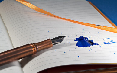 A copper fountain pen splats a blue ink mess on a notebook with orange bindings and ribbon - Powered by Adobe