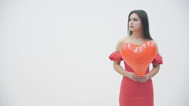 Slowmotion video of upset girl is holding a red heart balloon while thinking about unrequited love or breakup.