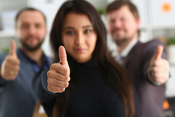 Portrait of pretty smiling young woman showing ok gesture with her male employees on the background