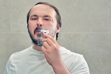 Adult man shaves his beard on his own, lifestyle. Concept of recovery and return to normal life after the coronavirus epidemic