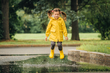 A girl in a yellow jacket and boots runs and jumps through puddles